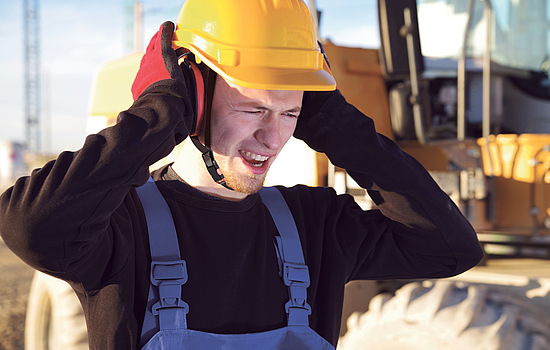 Mann steht auf einer Baustelle und drückt seinen Kapselgehörschutz gegen die Ohren.